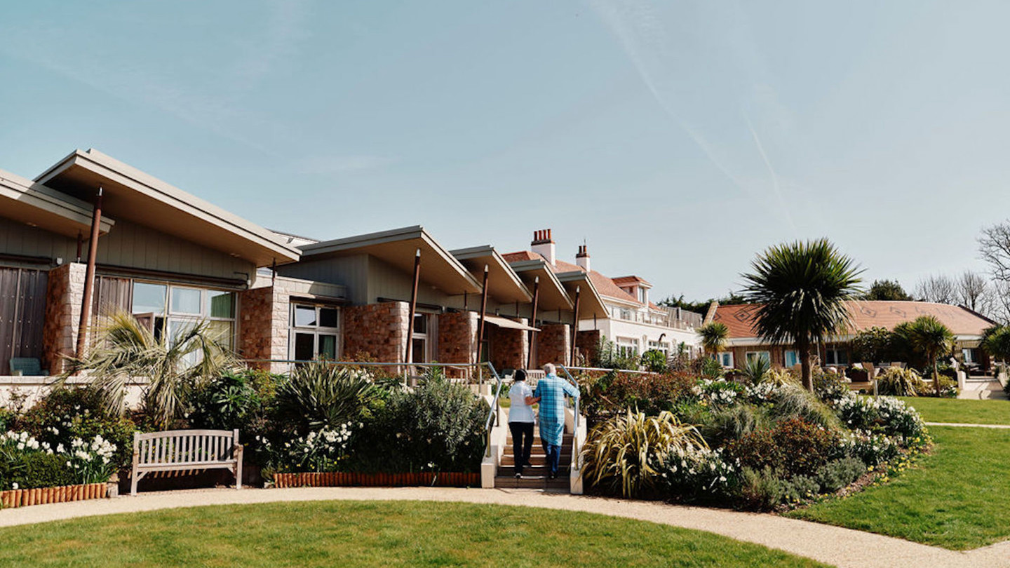 Image of nurse and patient walking up stairs in Hospice gardens with Hospice building behind them