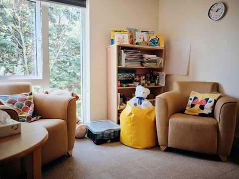 Image of bereavement room, two chairs and a table, with books in the corner and a teddy