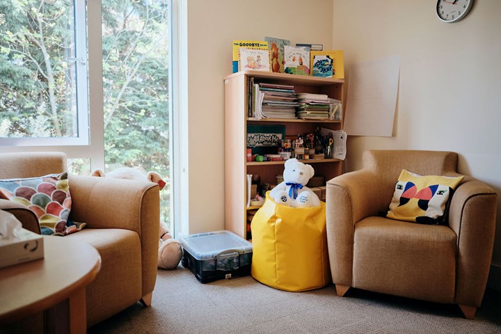 Image of bereavement room, two chairs and a table, with books in the corner and a teddy
