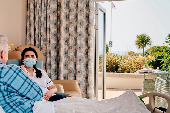 Image of patient in bed and nurse sat next to him 