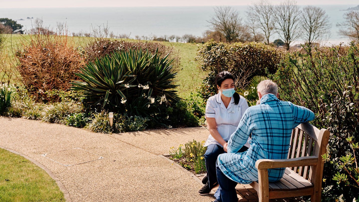 Image of nurse and patient sat on bench in gardens at Jersey Hospice Care