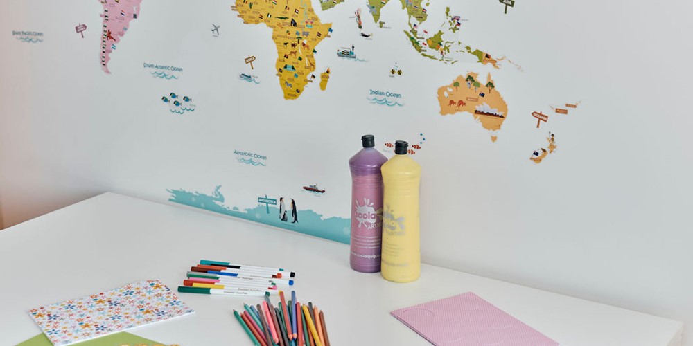 Image of desk with pens, paper, paint and stickers.  Map of the world on the wall