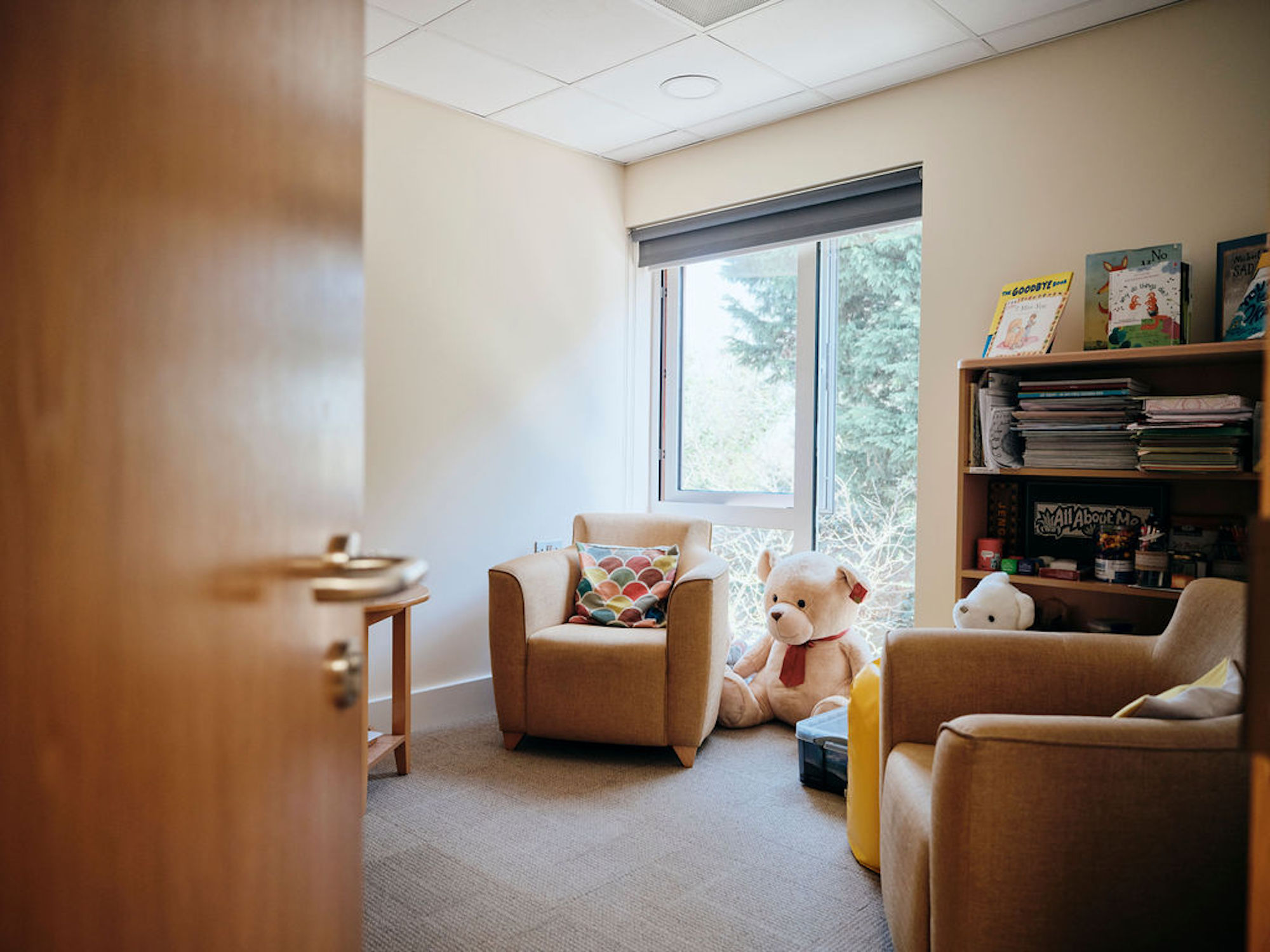 Image of bereavement room with door half open.  Two chairs and a table with large teddy in corner